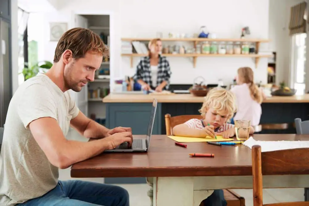 Working from home can cause a drop in water pressure from extended usage- Dad and son work at table while Mom and daughter work at kitchen island